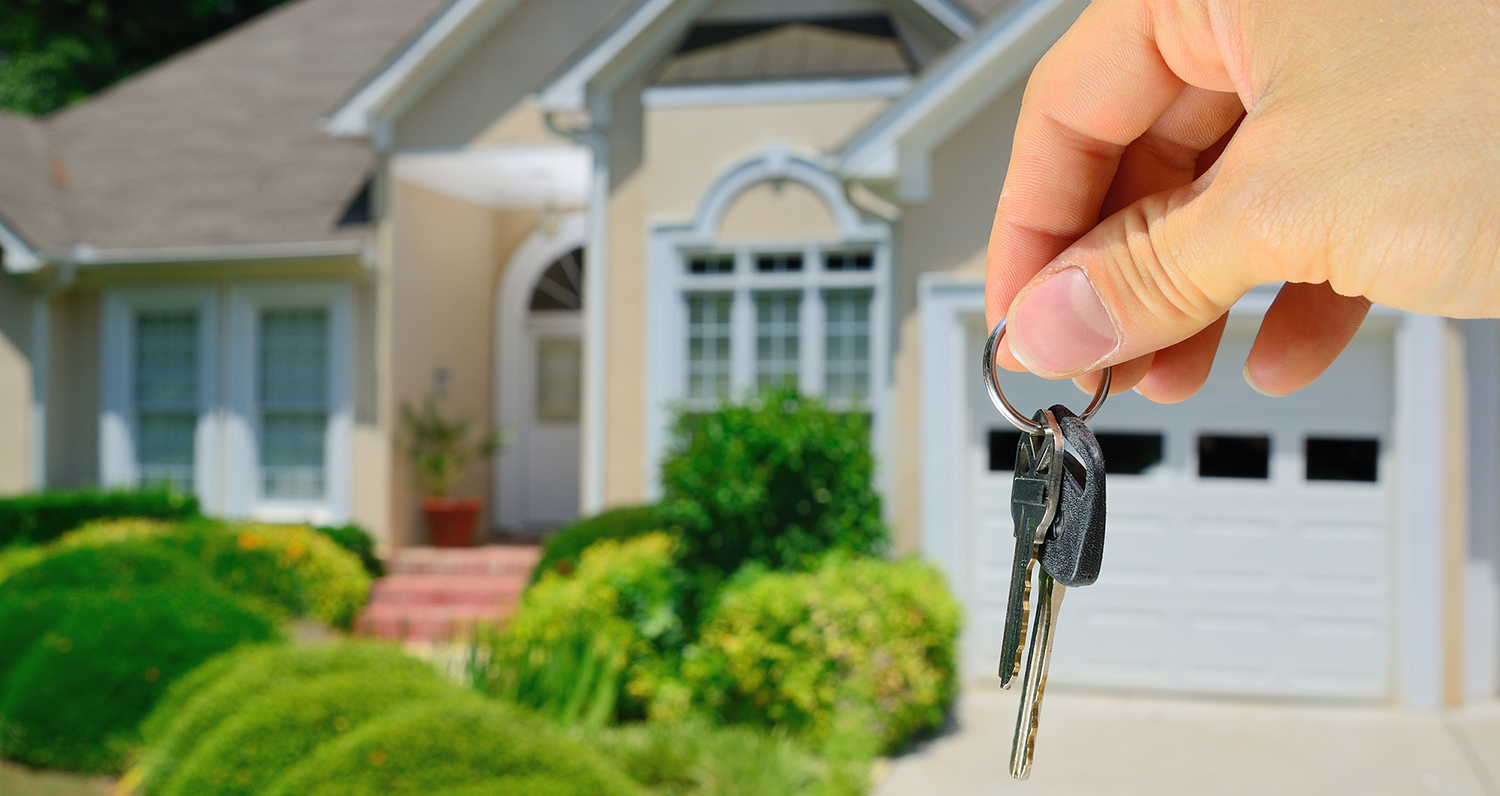 Hand holding house keys in font of a new residential property that just passed thorough home inspection services